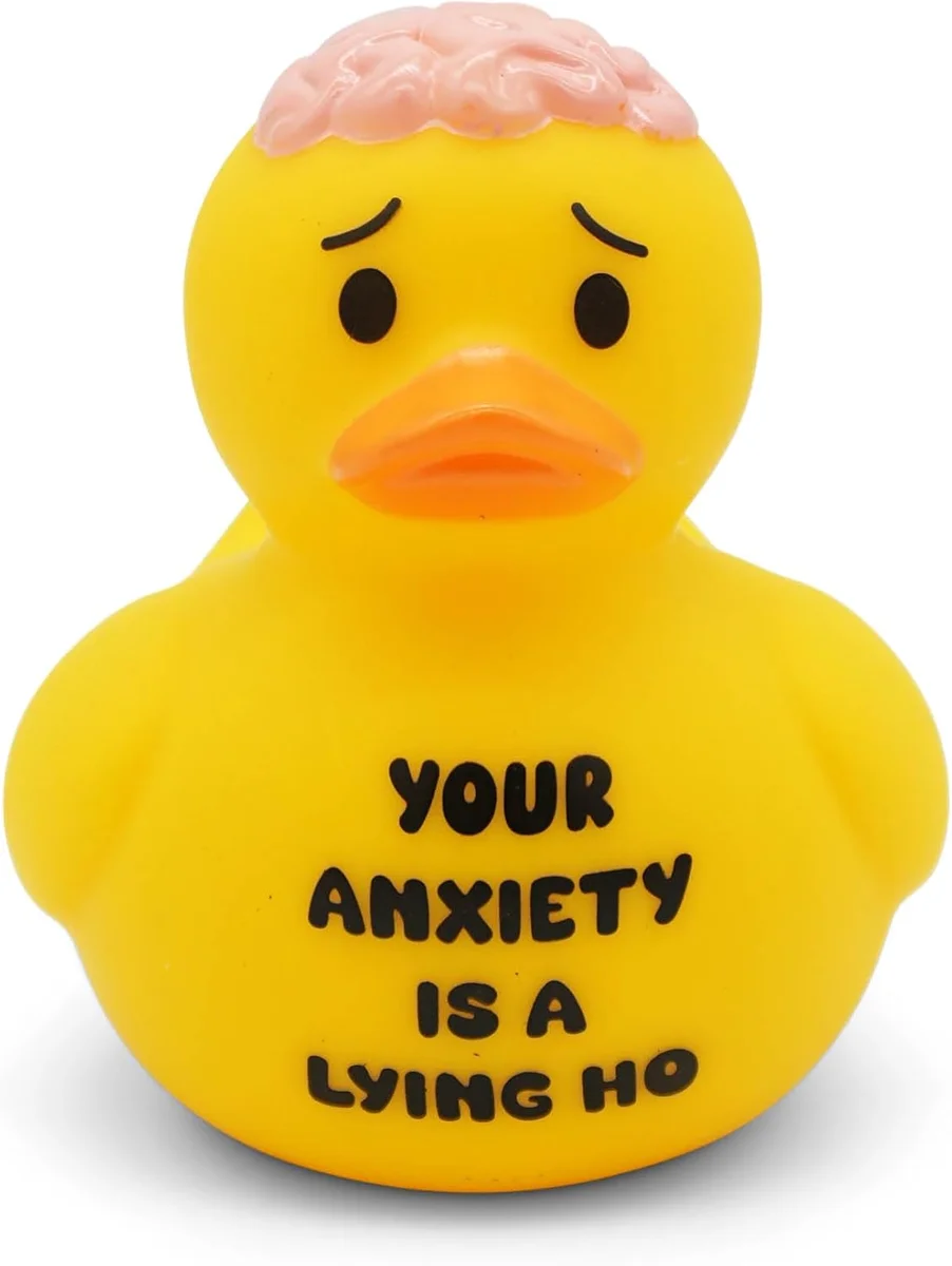 Small yellow rubber bath duck with an orange bill printed with the phrase "Your Anxiety is a Lying Ho" across its side in bold black text, roughly four inches tall