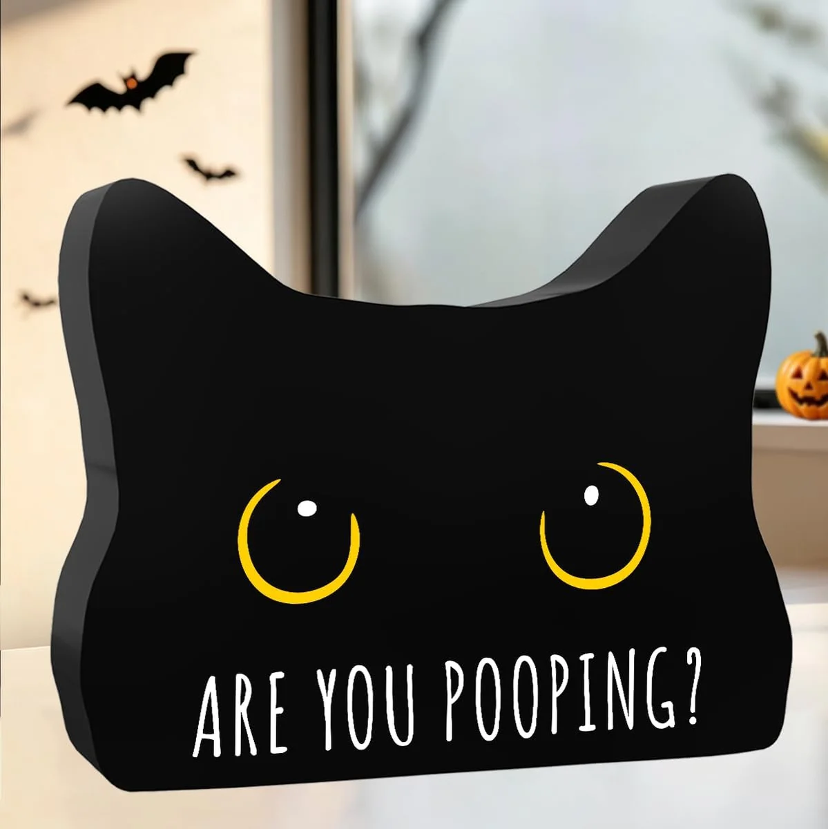 Black wooden bathroom decor sign shaped like a cartoon black cat with big yellow eyes peeking over the top, printed with the words 'Are You Pooping?' in white lettering, styled as Halloween-themed novelty bathroom art