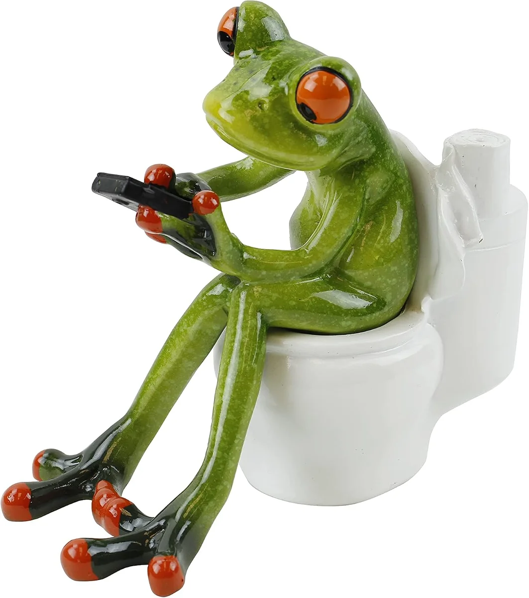 Green and black frog figurine sitting on a toilet holding a game controller